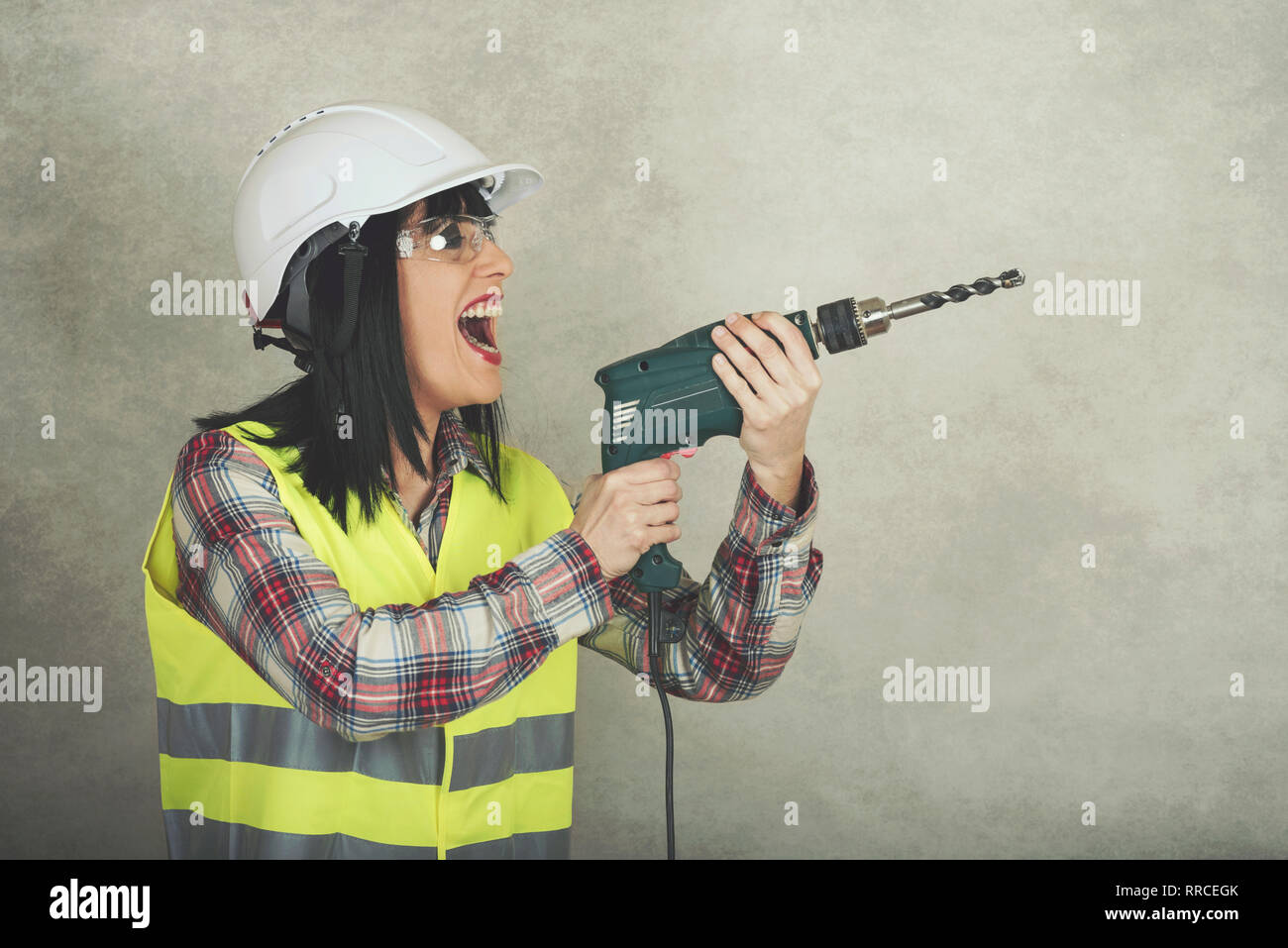 Donna lavoratore edile tenendo un trapano nelle sue mani contro lo sfondo grigio Foto Stock