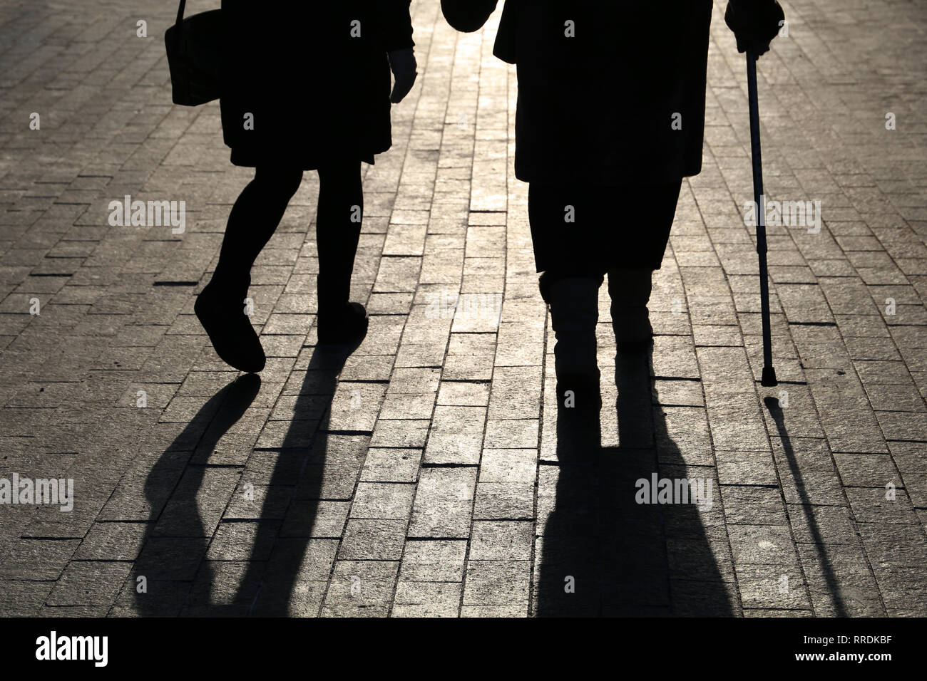 Ragazza e la donna con una canna da zucchero, silhouette nera e le ombre di due persone che camminano per la strada. Concetto di zoppicante, vecchiaia, anziani o non vedente Foto Stock