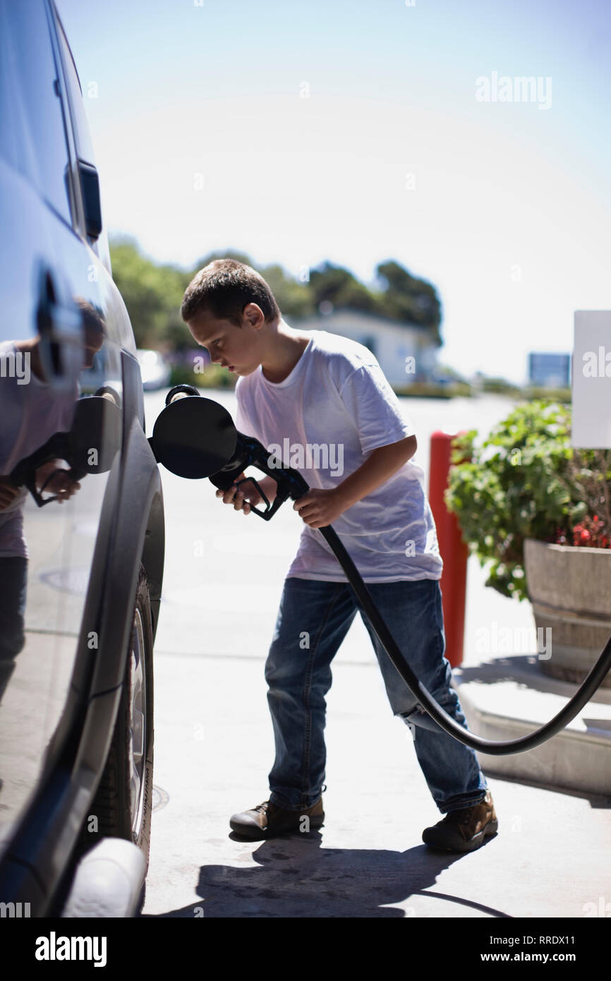 Ragazzo inserendo un tubo del combustibile all'interno di un'auto in una stazione di benzina. Foto Stock