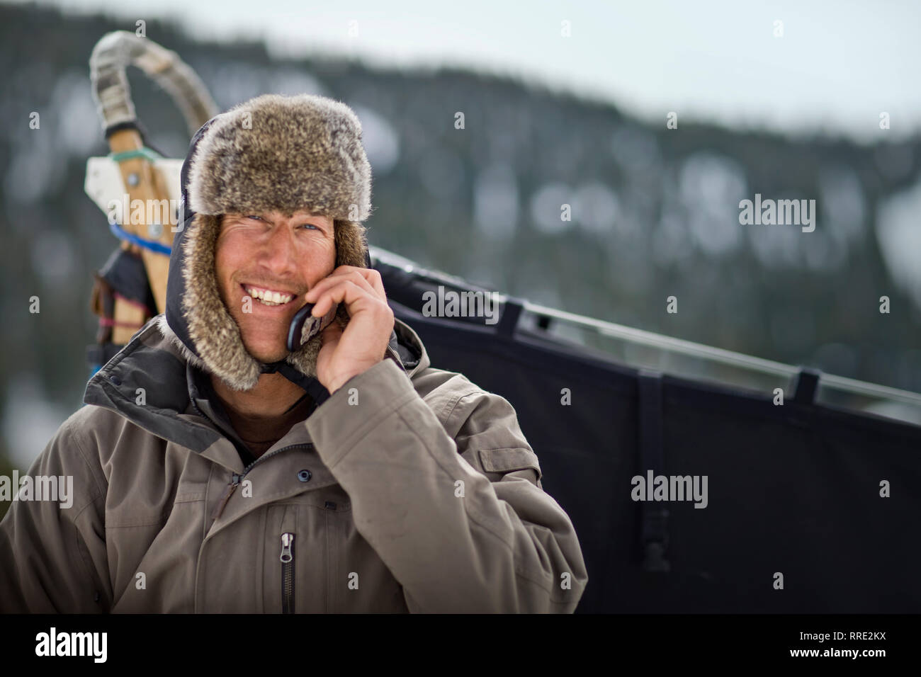 Ritratto di un sorridente metà uomo adulto parlando sul suo telefono cellulare mentre in piedi all'aperto indossando un cappello di pelliccia. Foto Stock