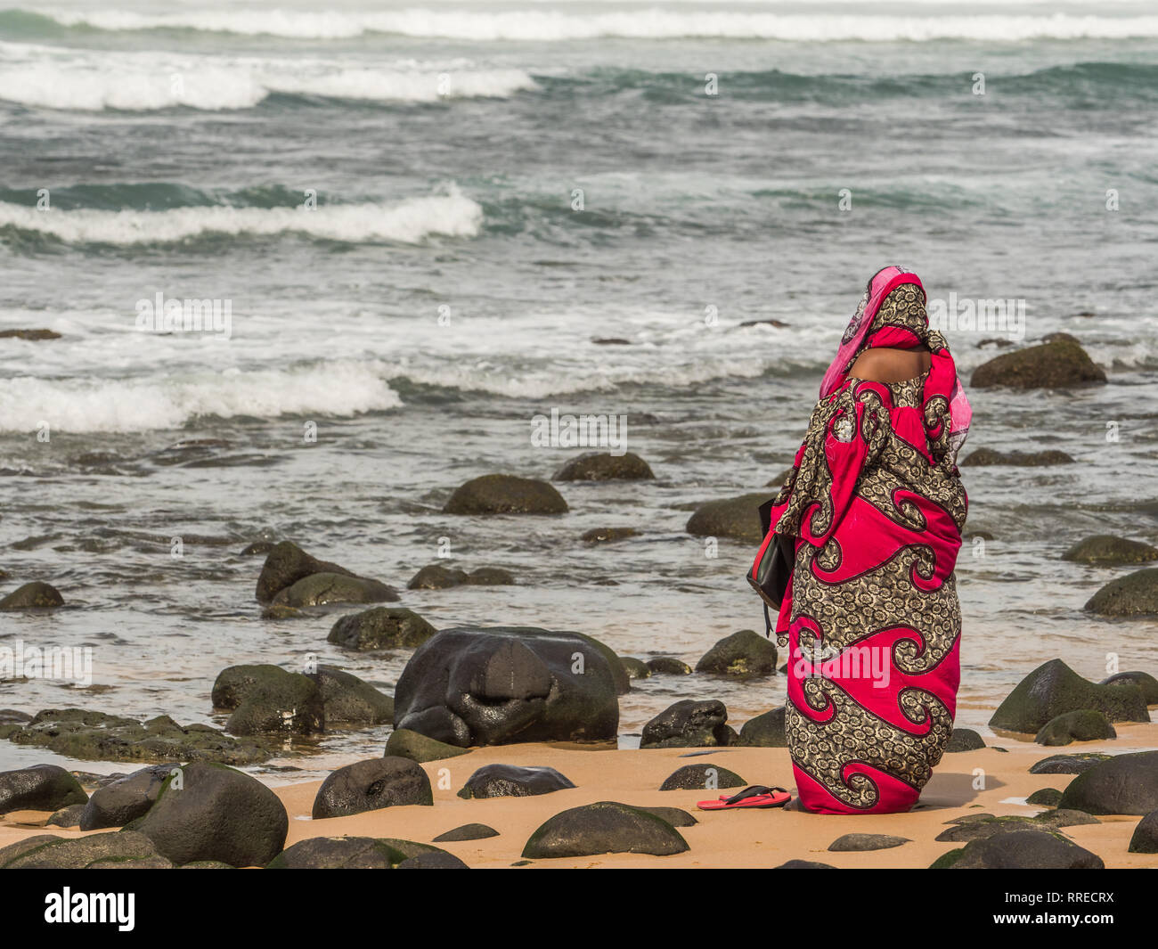 Una figura di una donna musulmana in un rosso boubou pregando in ocean shore. Il Senegal. L'Africa. Foto Stock