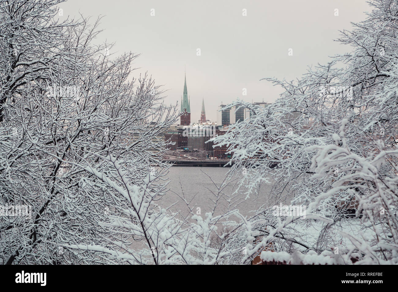 Città di Stoccolma e due torri della chiesa visibile attraverso i boschi dell'altro lato del fiume su una giornata invernale con un po' di neve, Seden Foto Stock