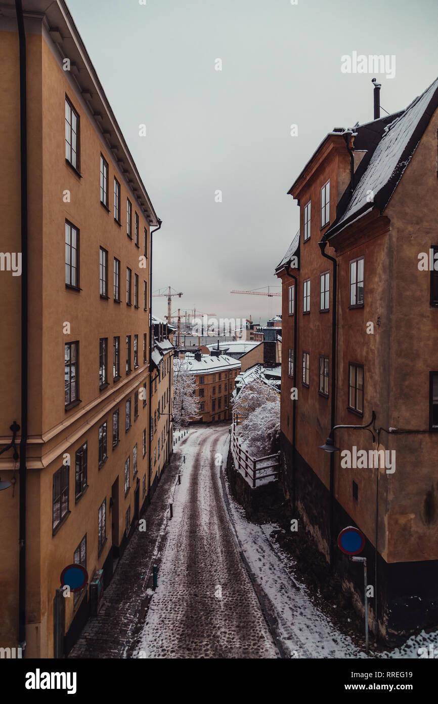 Stretta strada vuota con vecchi edifici in un giorno di inverno con la neve con il fiume in background, Stoccolma Svezia Foto Stock