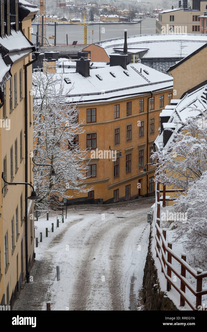 Stretta strada vuota con vecchi edifici in un giorno di inverno con la neve con il fiume in background, Stoccolma Svezia Foto Stock