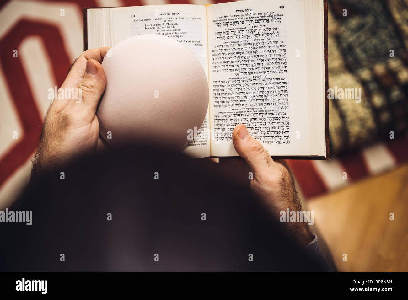Vista da sopra del maschio ebreo holding kippa , lettura orante bi-lingue ebraico mahzor francese libro di preghiera da 1920 utilizzato in alto i Giorni santi di Rosh Hashanah e Yom Kippur Foto Stock