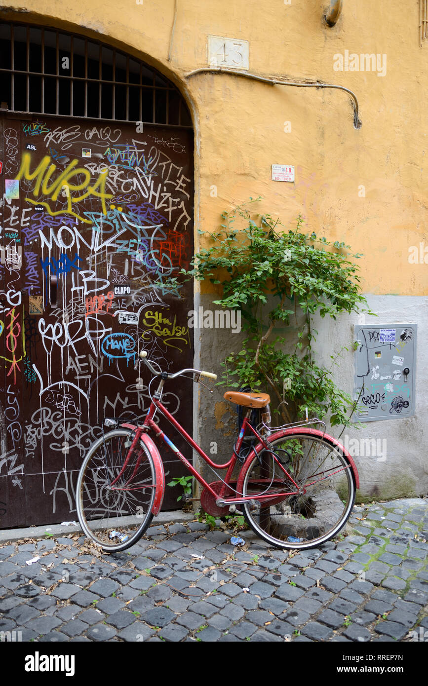 Scena di strada con parcheggio biciclette rosse e coperto di graffiti muri color ocra nell'elegante e storico quartiere di Trastevere Roma Italia Foto Stock
