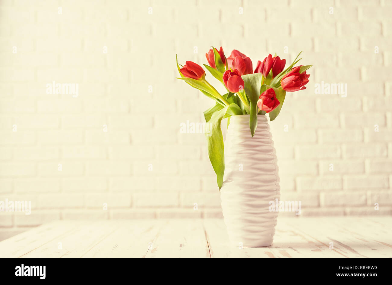 Tonificazione retrò di tulipani in un vaso bianco contro il bianco sullo sfondo di mattoni Foto Stock