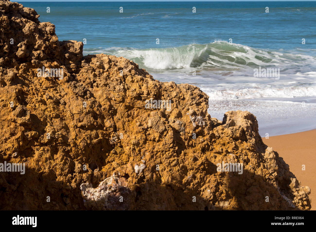 Rocce sulla spiaggia pulita con giallo scuro sabbia. Le onde spumeggianti dell'Oceano Atlantico. Orizzonte in background. Cielo blu chiaro. Lalla Fatna spiaggia (Safi) Foto Stock