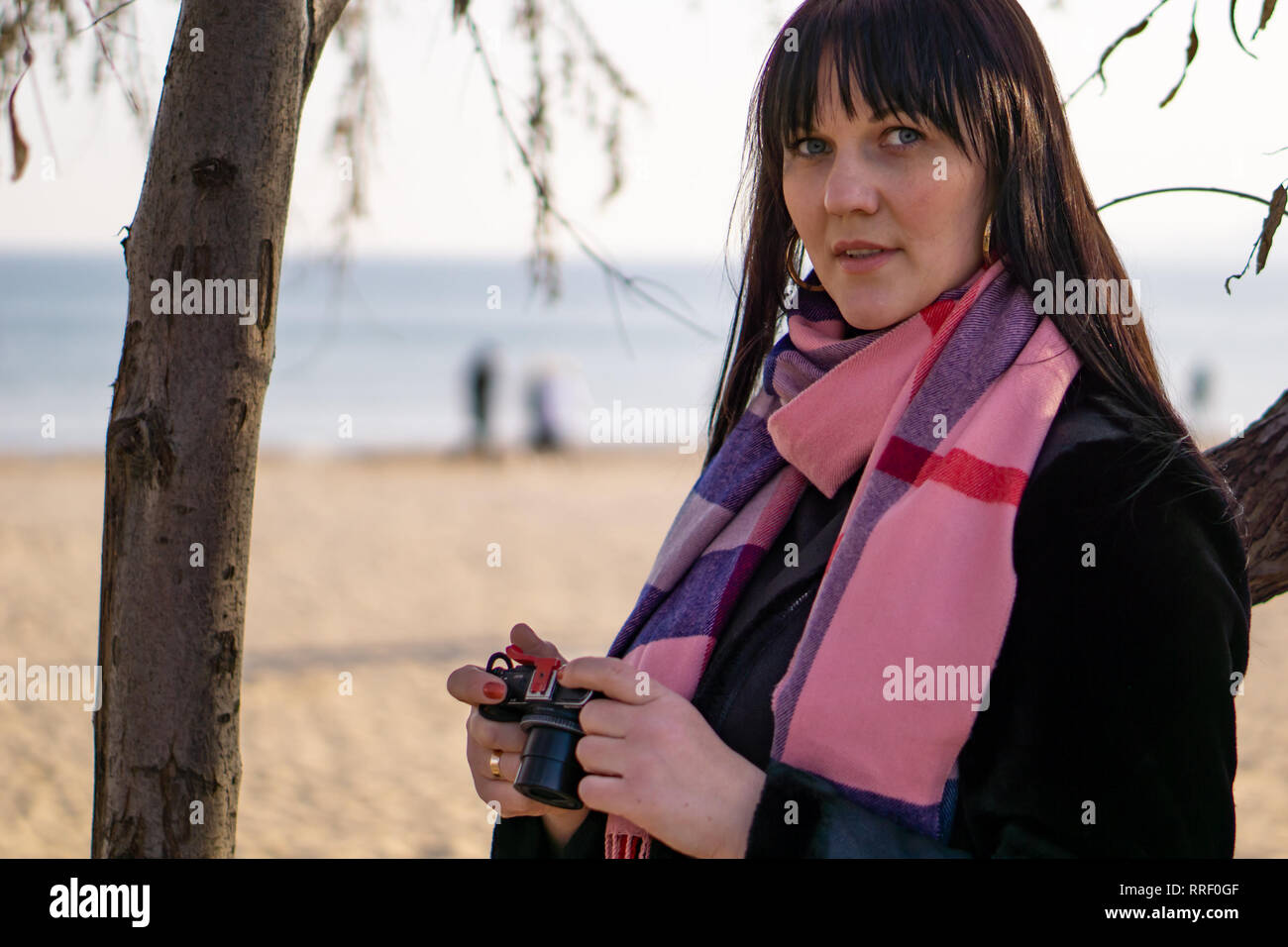 Bella bruna donna in una sciarpa rosa con una telecamera dal mare su una soleggiata giornata di primavera. Foto Stock