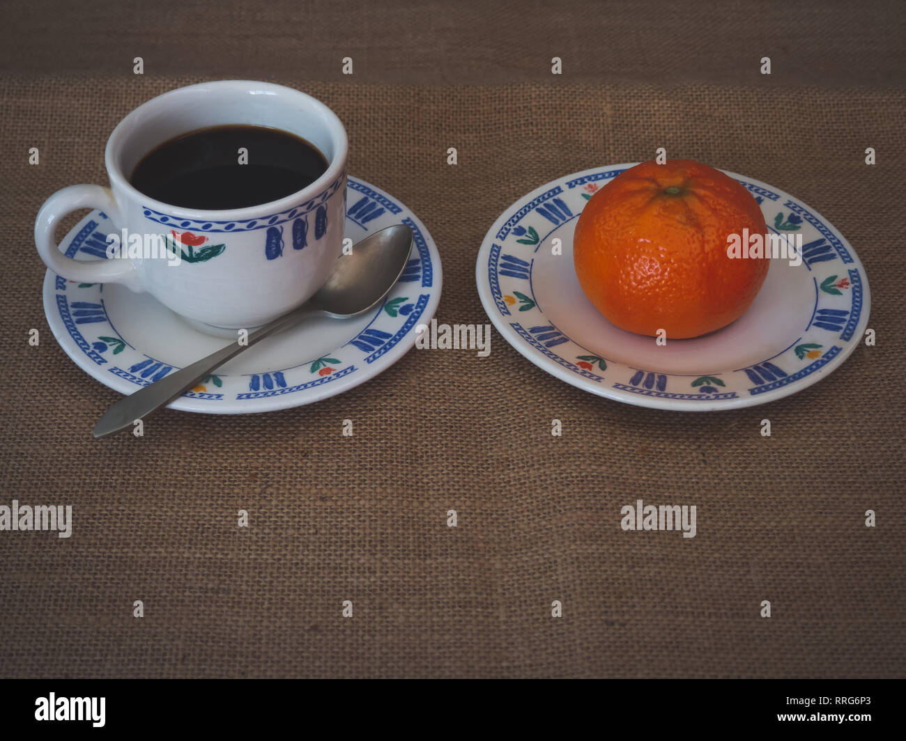La prima colazione di una tazza in porcellana, un vecchio cucchiaio e una piastra con un mandarino su una tela vintage background Foto Stock