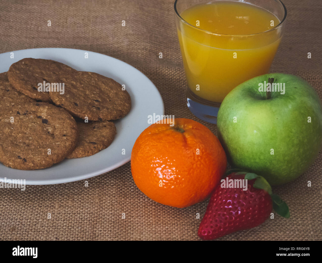 La prima colazione a partire da un vetro con succo di arancia di mandarino, una mela verde e una piastra con i cookie su una tela vintage background Foto Stock