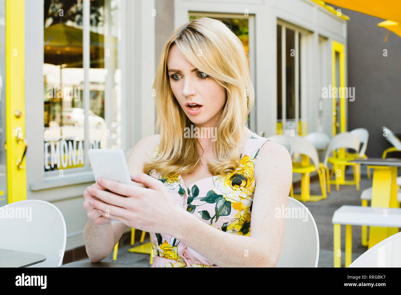 Ragazza con espressione scioccata guarda al suo telefono cellulare a un cafe' all'aperto Foto Stock