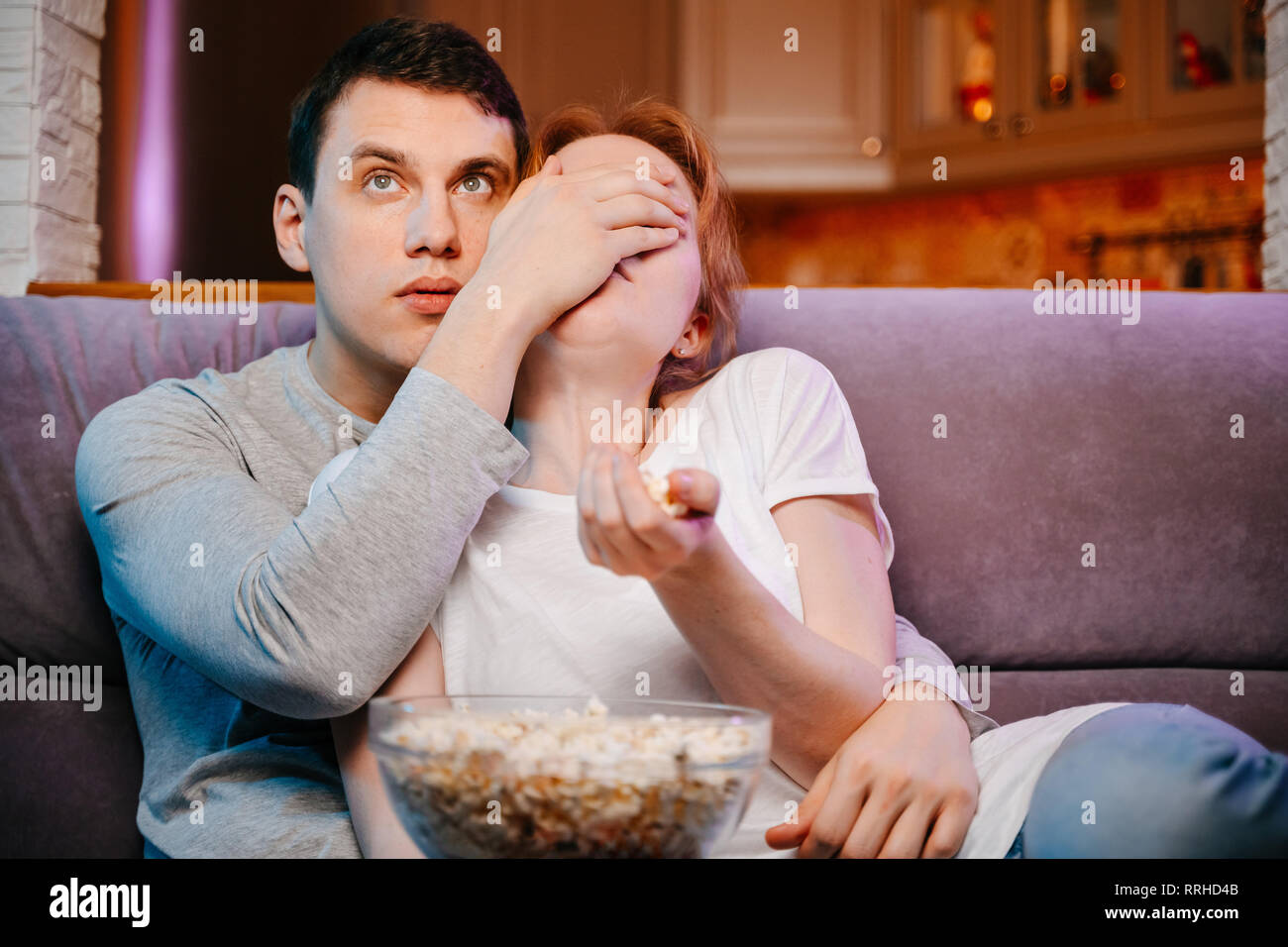 Coppia giovane mangiare popcorn e guardare un film a casa sul lettino, spaventata. Foto Stock