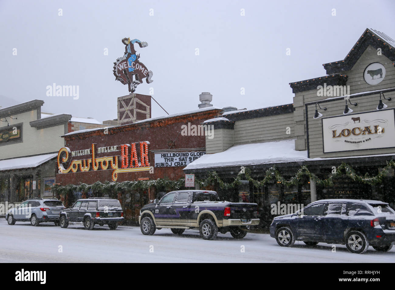 Million Dollar Cowboy Bar segno di benvenuto e automobili su un nevoso, giornata invernale nella parte occidentale della città di Jackson, Wyoming Dicembre 24, 2018 Foto Stock