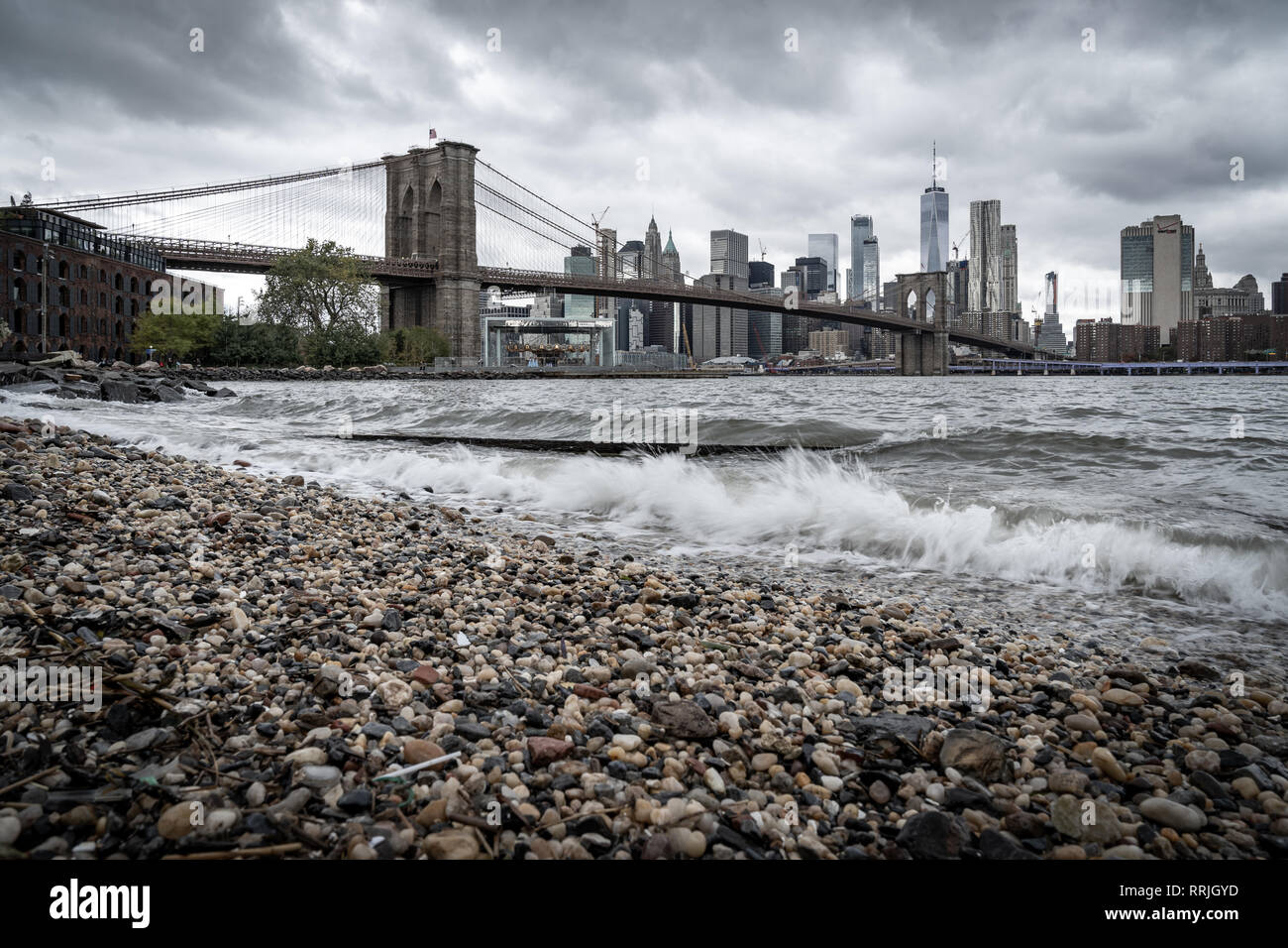 Una spiaggia di ciottoli sull'East River a Brooklyn guardando verso il ponte di Brooklyn e la parte inferiore di Manhattan, New York, Stati Uniti d'America Foto Stock