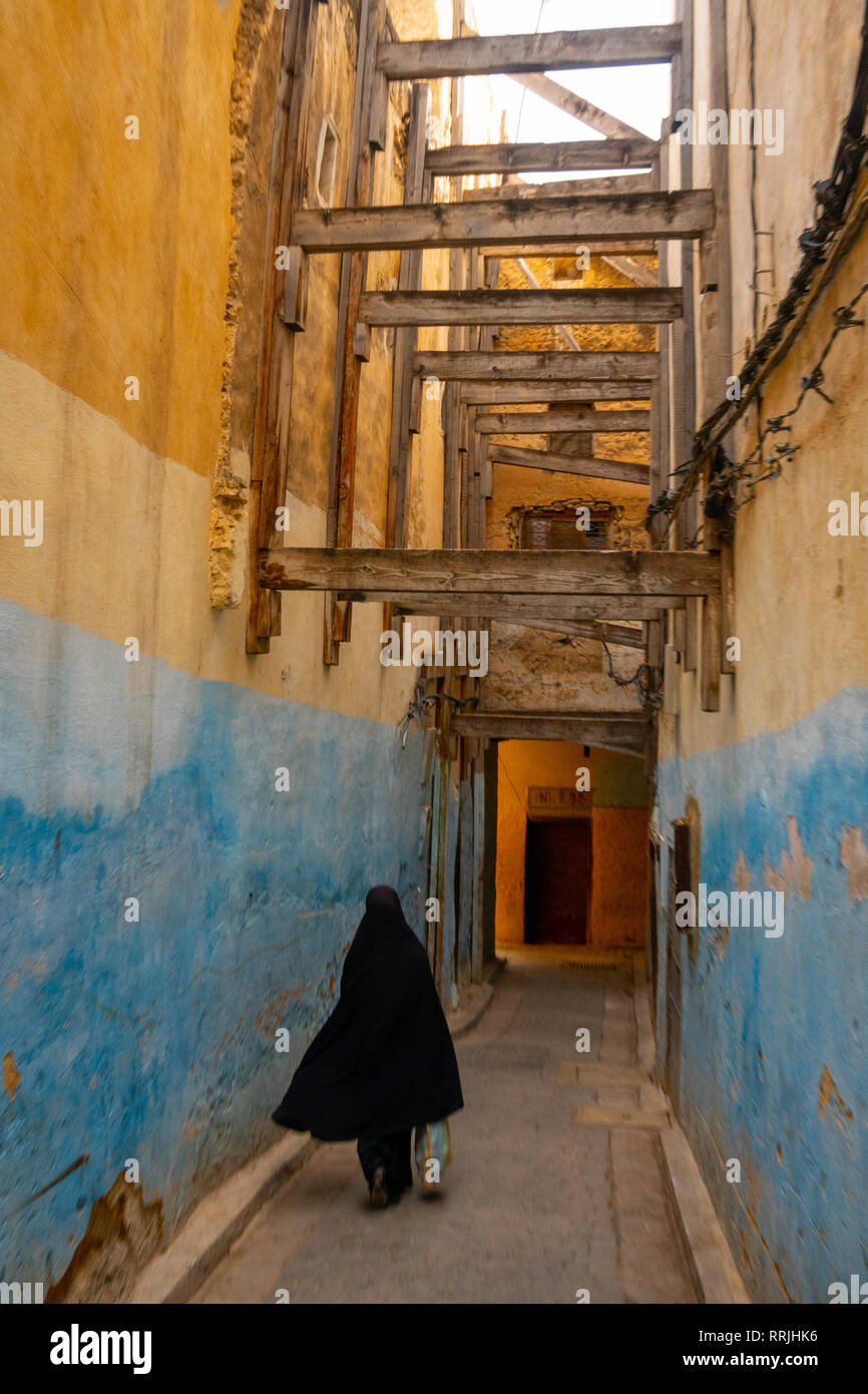 La donna in nero vestito tradizionale scompare giù un vicolo colorato nella Città Vecchia (Medina di Fez, Marocco, Africa Settentrionale, Africa Foto Stock