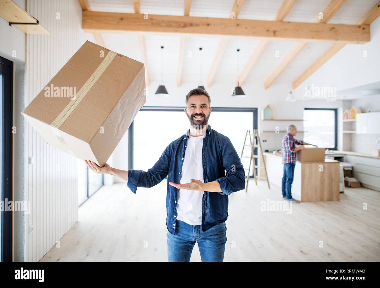 Un uomo maturo tenendo una grande scatola in una mano nell'arredamento di casa nuova, un nuovo concetto di casa. Foto Stock