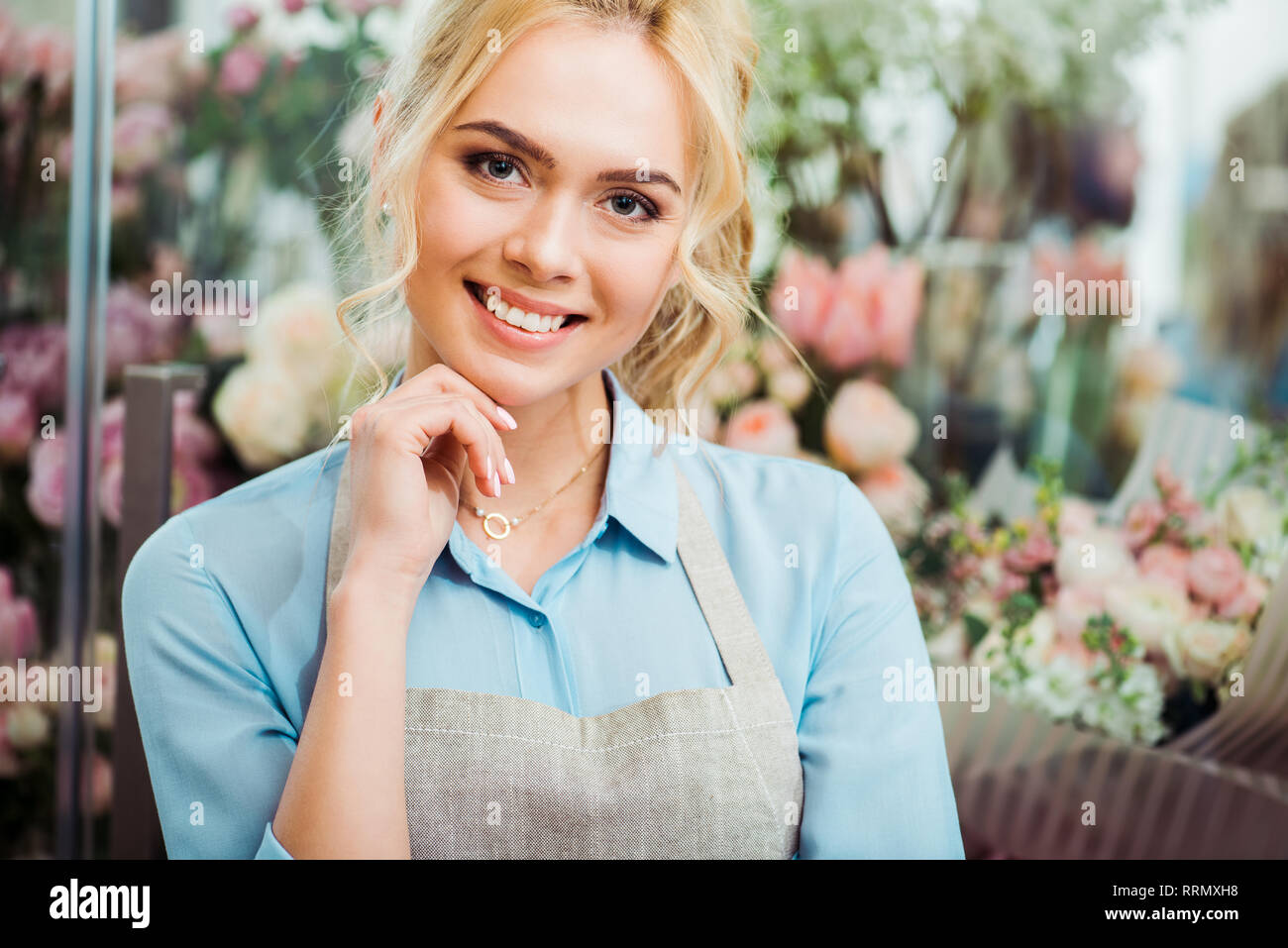 Bellissima femmina fioraio in grembiule toccando ching e sorridente con negozio di fiori su sfondo Foto Stock
