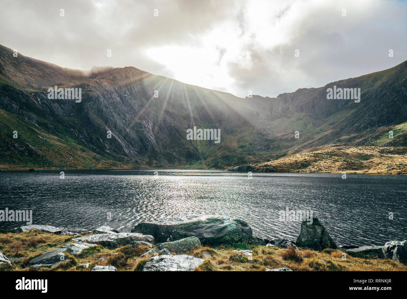Sole che splende su tranquillo lago e monti, Snowdonia NP, REGNO UNITO Foto Stock