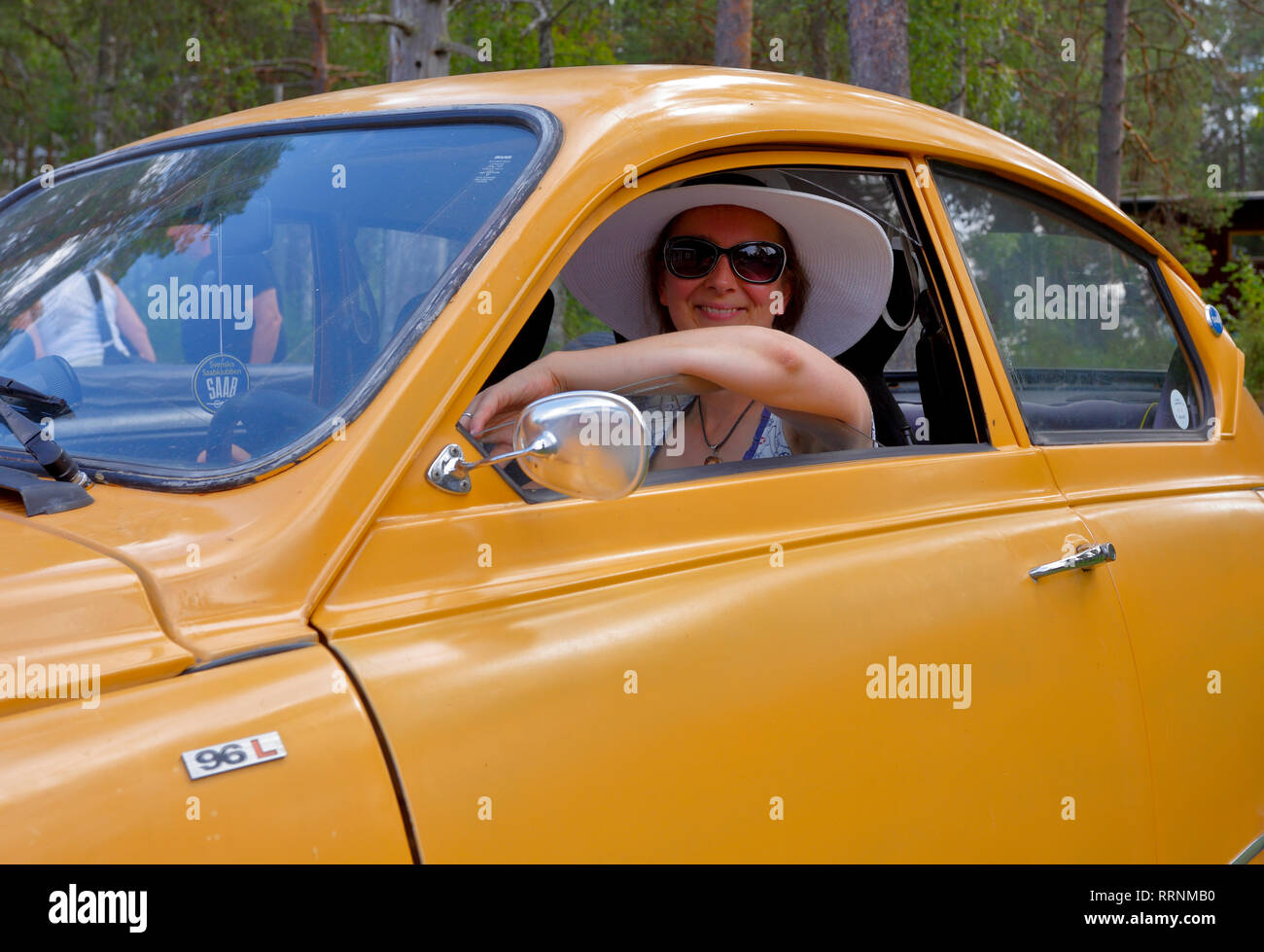 Giovane donna indossa wide-colmato cappello bianco e occhiali da sole al volante di un'annata Saab 96 Foto Stock