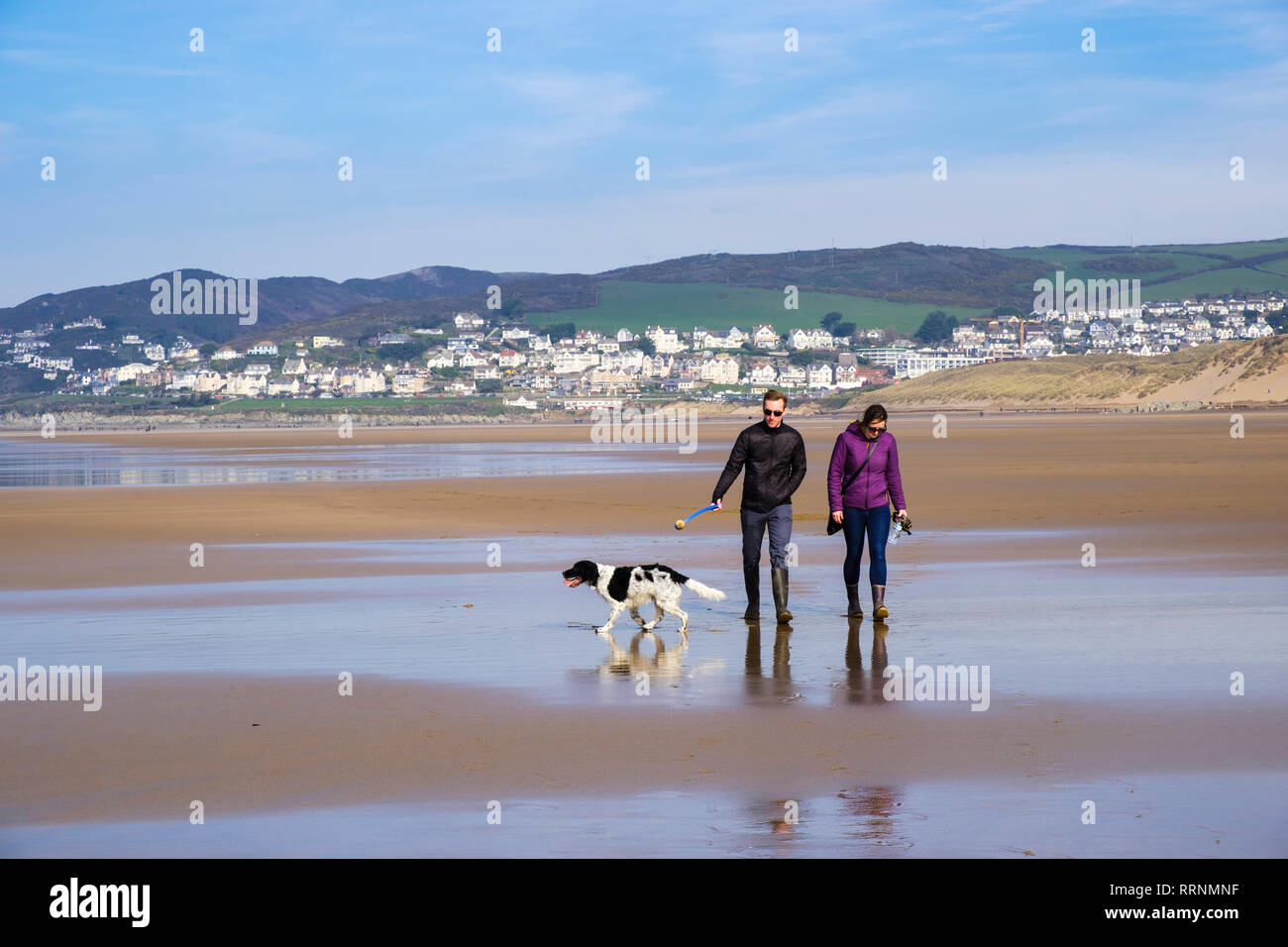 Una coppia millenaria di persone che camminano un cane Springer Spaniel sulla tranquilla spiaggia sabbiosa con bassa marea in inverno. Woolacombe nord Devon Inghilterra Regno Unito Gran Bretagna Foto Stock