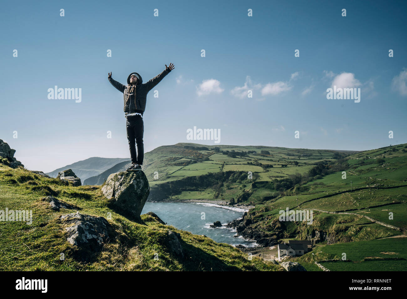 Carefree uomo in piedi sulla roccia che si affaccia soleggiato, paesaggio idilliaco, Irlanda del Nord Foto Stock