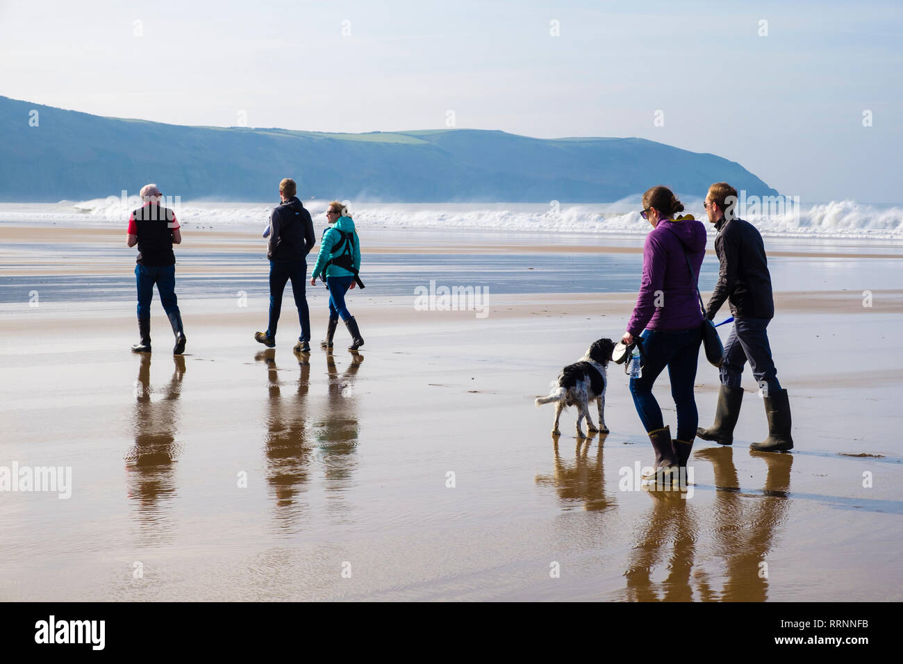 Un gruppo di persone con un cane a camminare su una tranquilla spiaggia di sabbia dall'Oceano Atlantico con la bassa marea. Woolacombe, North Devon, Inghilterra, Regno Unito, Gran Bretagna Foto Stock