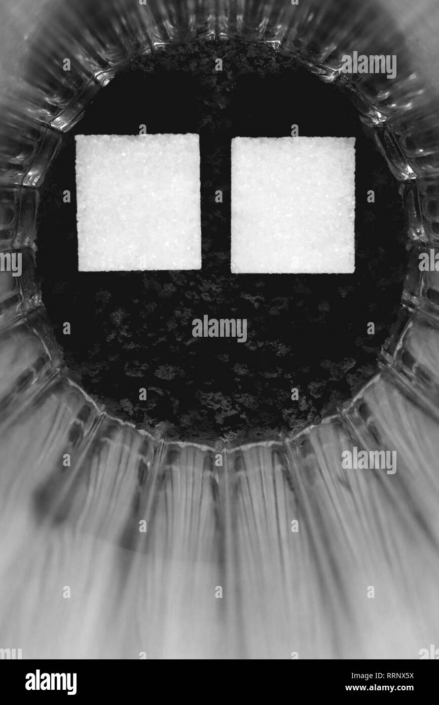 Due pezzi di zucchero in un bicchiere con un caffè insolubile. In bianco e nero. Foto Stock