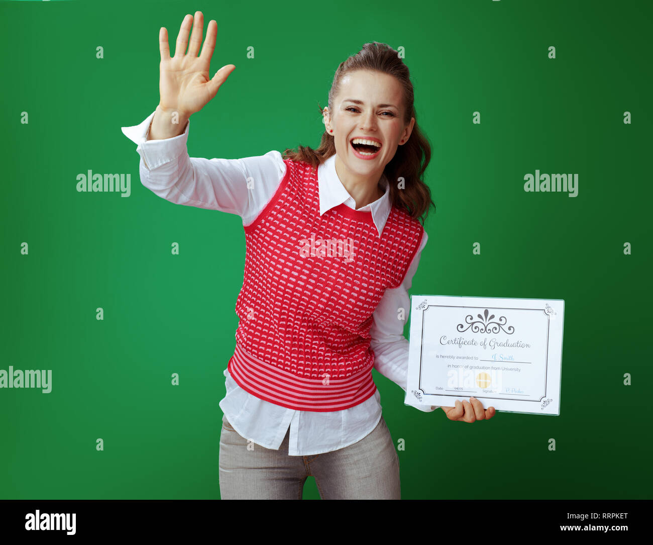Sorridente studente moderno in jeans grigio e rosa camicia senza maniche con Certificato di diploma accogliente contro lo sfondo di colore verde. nuovo dipendente nel Foto Stock