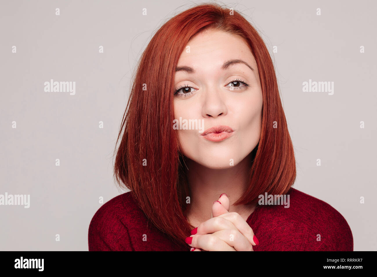 Piuttosto giovane donna con i capelli rossi nel bordo camicetta tenendo le sopracciglia e invio di bacio. Foto Stock