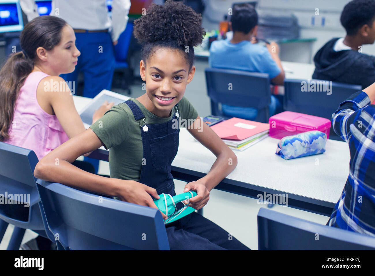 Ritratto sorridente, fiduciosi junior high school girl studente con le cuffie al banco in aula Foto Stock