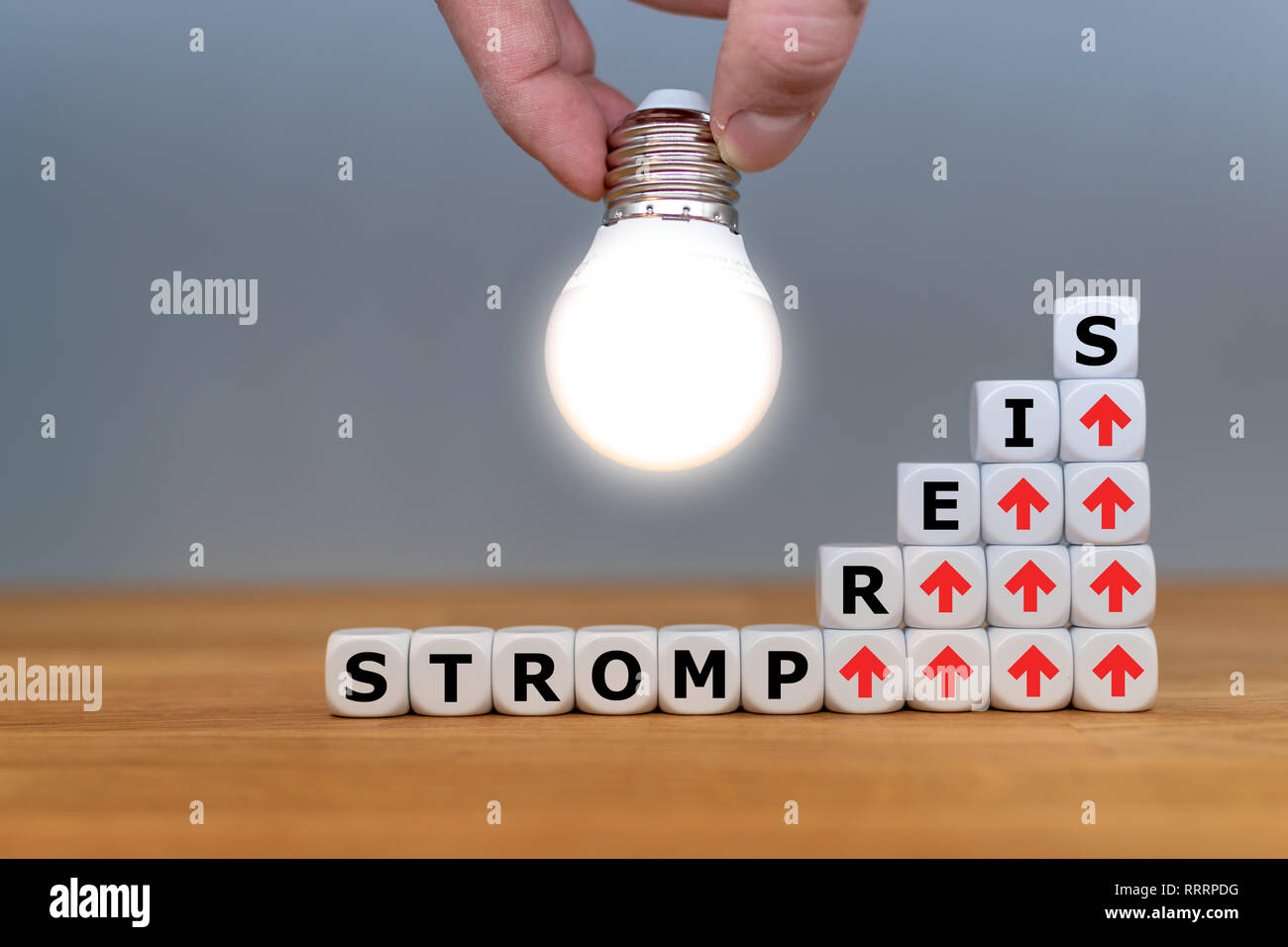 Simbolo per aumentare i tassi di elettricità. Dadi formano la parola tedesca "trompreis" ("tasso di elettricità" in inglese) nella parte anteriore di una lampadina. Foto Stock