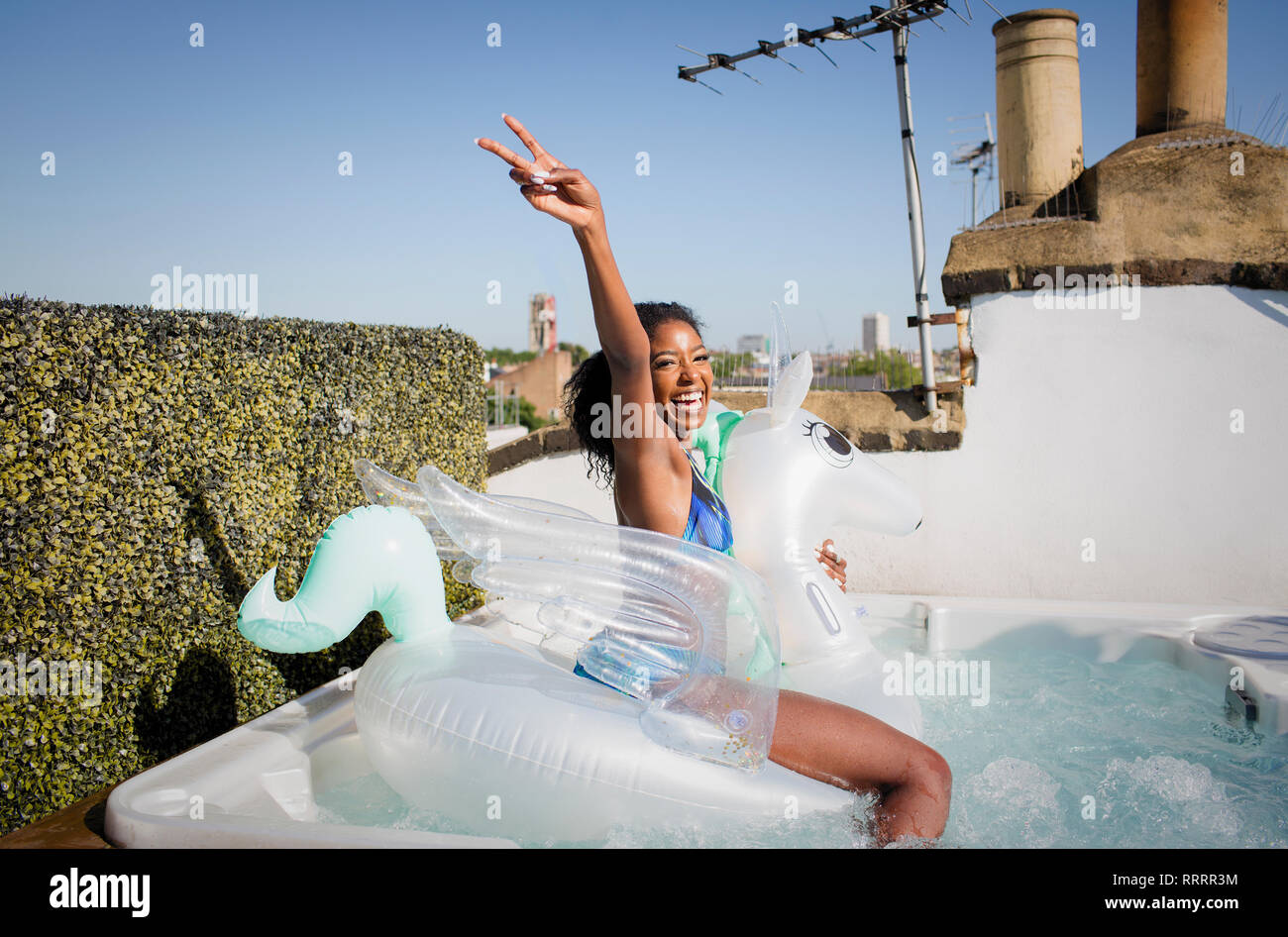 Ritratto giocoso, fiducioso giovane donna seduta su Pegasus gonfiabile nella soleggiata terrazza sul tetto la vasca calda Foto Stock