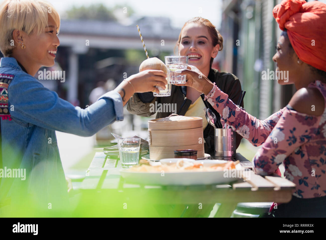 Donne giovani amici di tostatura bicchieri di acqua a pranzo dim sum a sunny cafè sul marciapiede Foto Stock