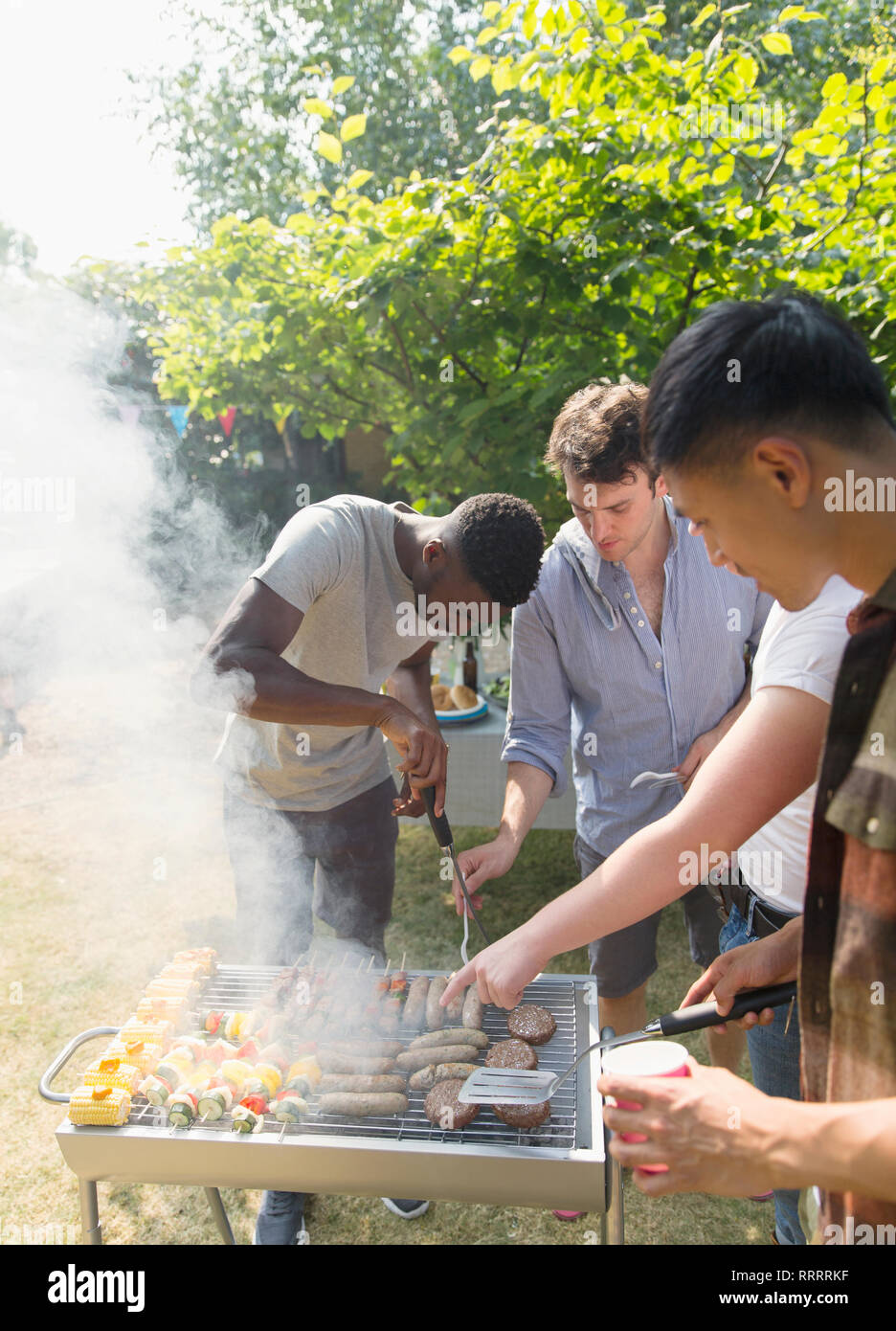 Amici di sesso maschile al grill barbecue nel cortile soleggiato Foto Stock