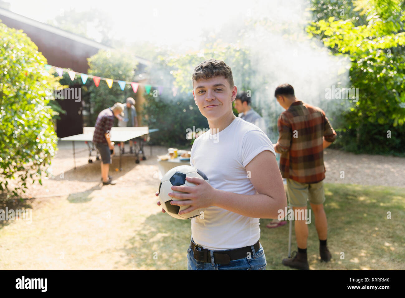Ritratto fiducioso ragazzo adolescente con pallone da calcio, godendo di backyard barbecue Foto Stock