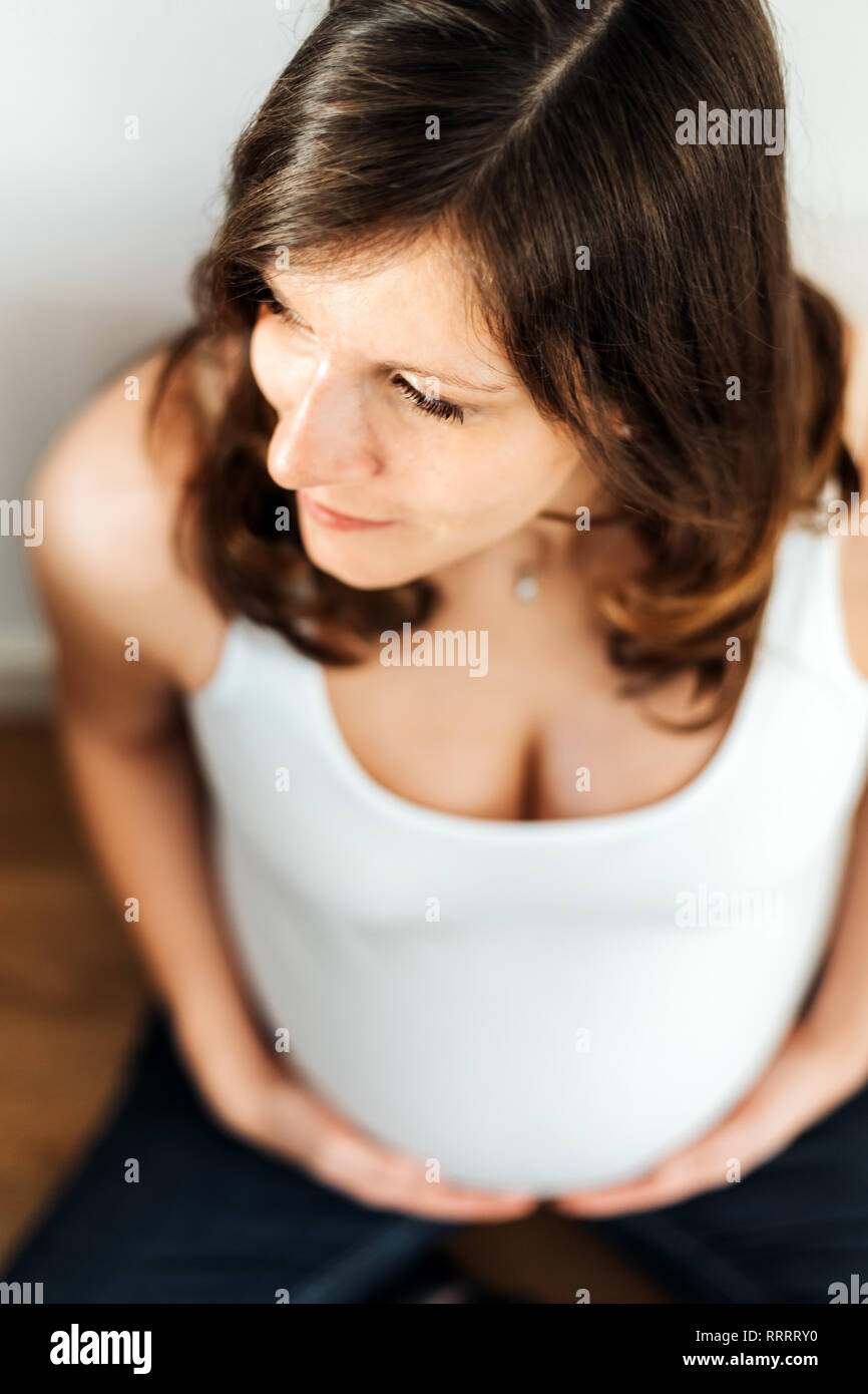 Elevato angolo di visione della donna incinta in maglia bianca tenendo il suo ventre Foto Stock