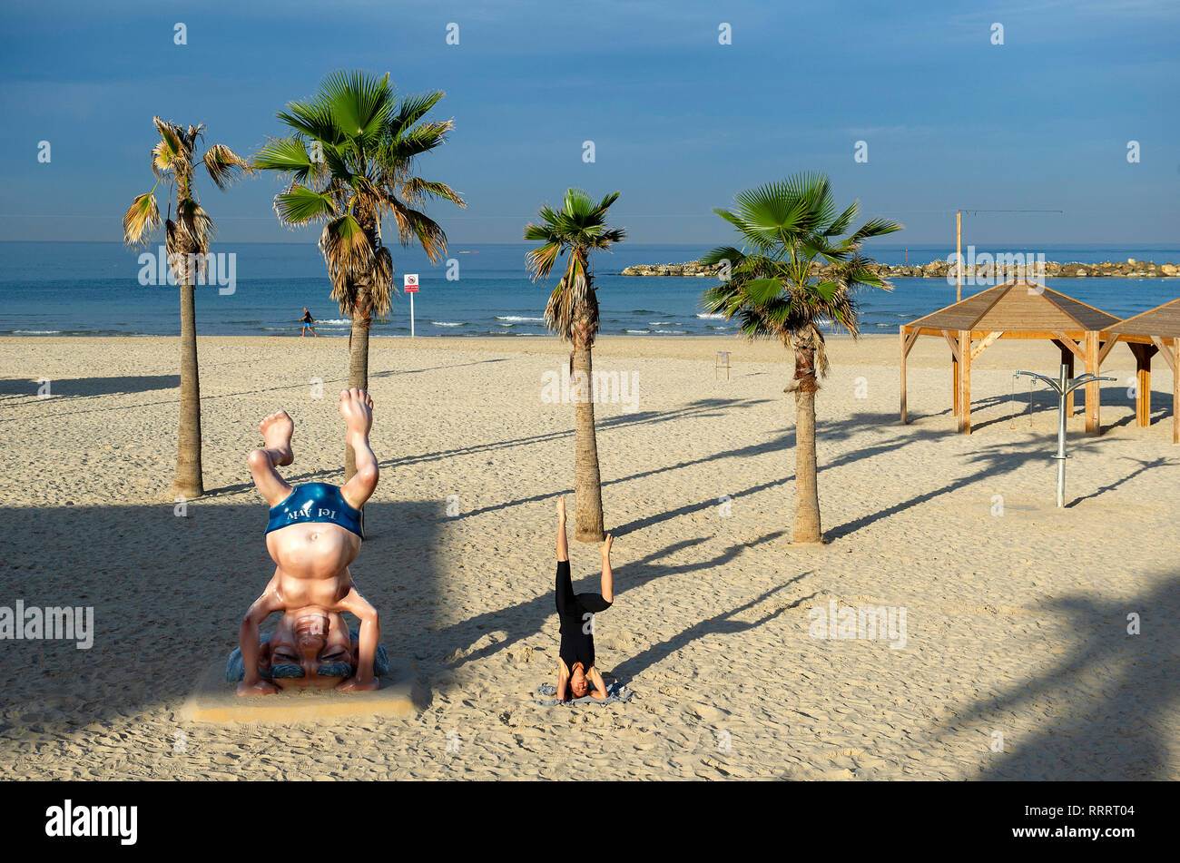 Giovane donna facendo un headstand accanto al Ben Gurion statua sulla spiaggia di Tel Aviv, Israele Foto Stock