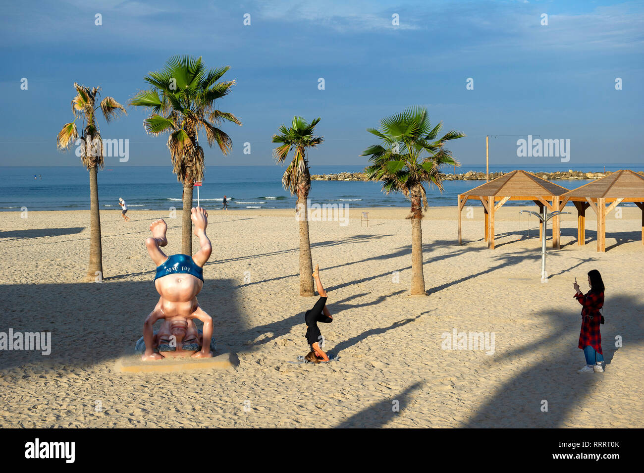 Giovane donna di scattare una foto del suo amico facendo un headstand accanto al Ben Gurion statua sulla spiaggia di Tel Aviv, Israele Foto Stock