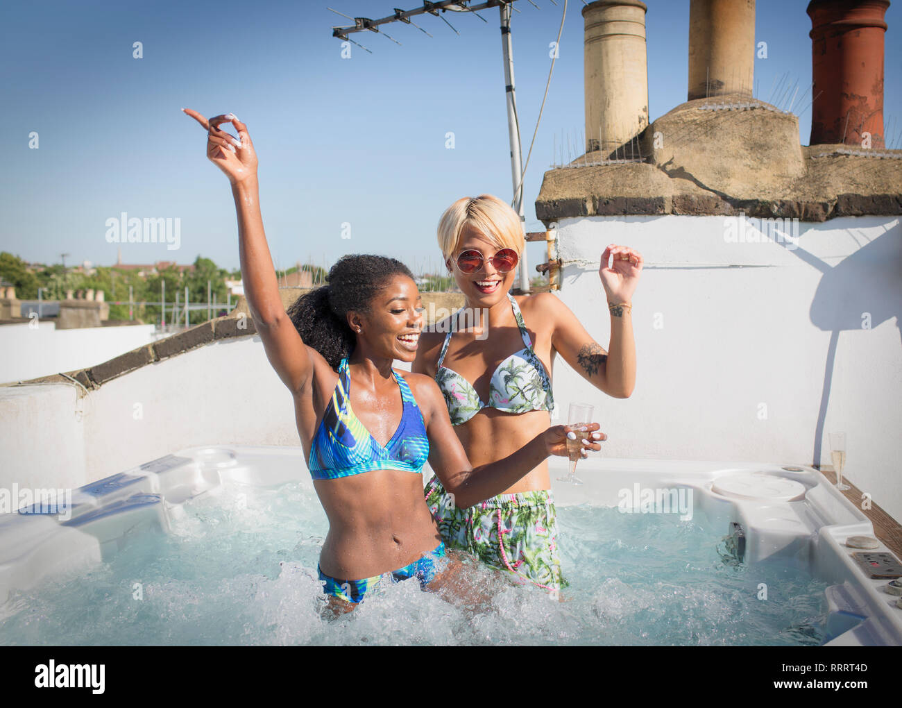 Ritratto giocoso donne giovani amici in bikini dancing nella soleggiata terrazza sul tetto la vasca calda Foto Stock