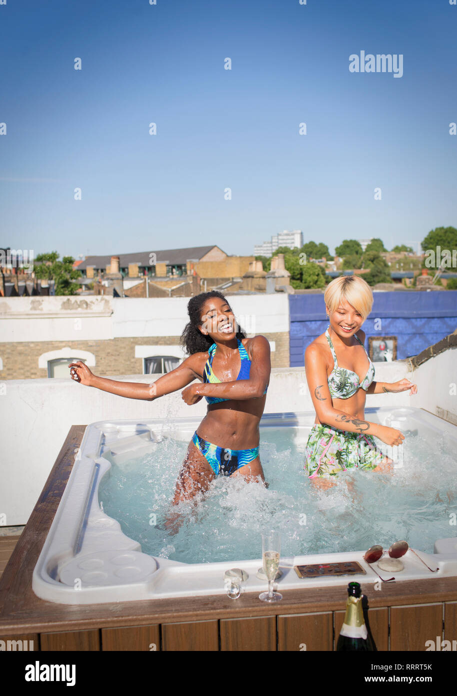 Giocoso donne giovani amici in bikini dancing nella soleggiata terrazza sul tetto la vasca calda Foto Stock