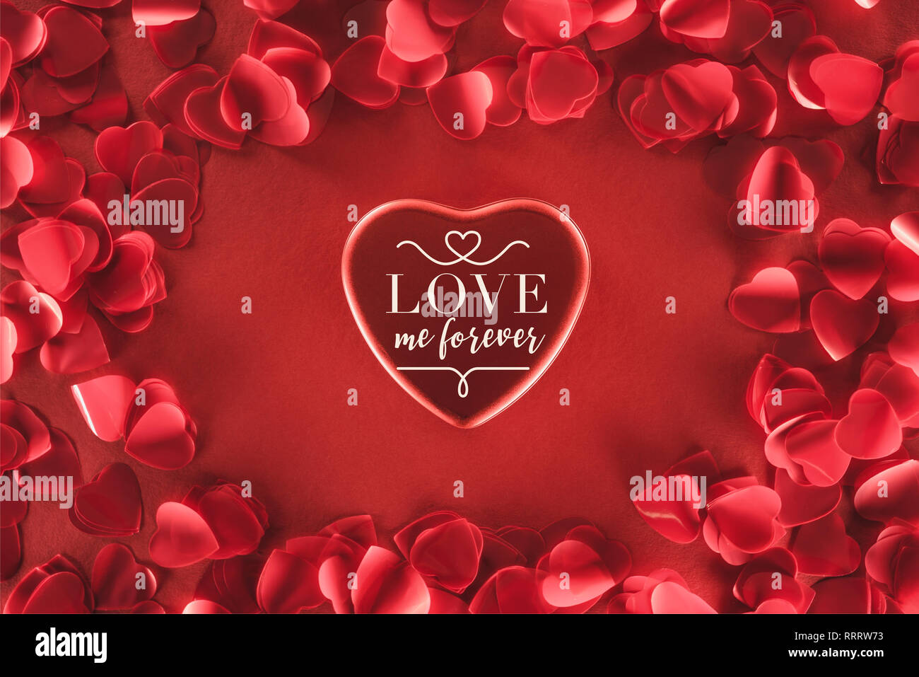 Vista superiore del bel cuore con "love me forever" scritte e petali di decorativo su sfondo rosso, il giorno di san valentino concetto Foto Stock