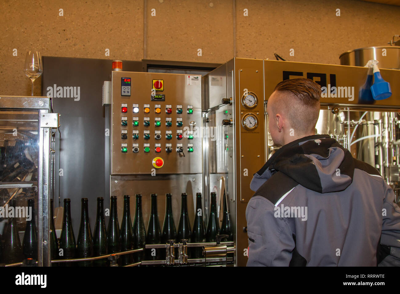 Un vignaiolo controlla le funzioni di una stazione di riempimento mentre whitewine imbottigliamento in bottiglie verdi Foto Stock