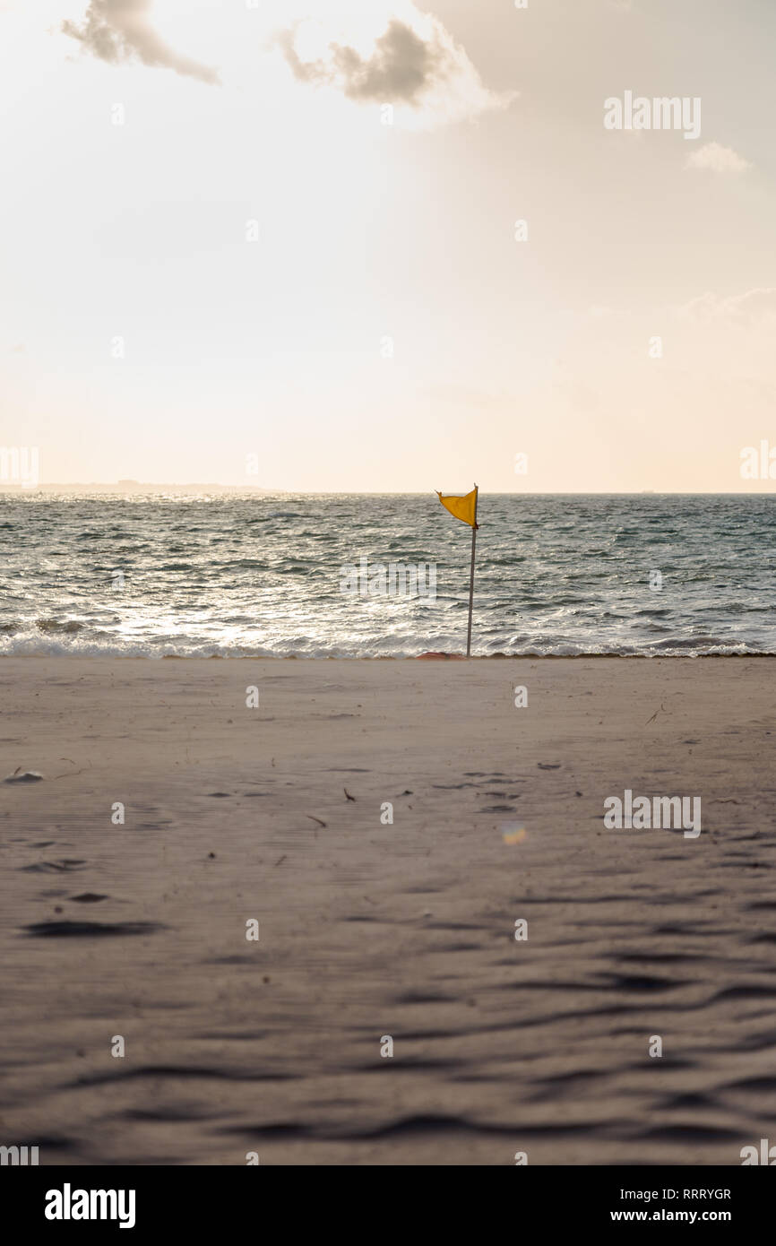 Un avviso di colore giallo flag indicanti condizioni avverse su un tropicale di spiaggia di sabbia bianca. Foto Stock
