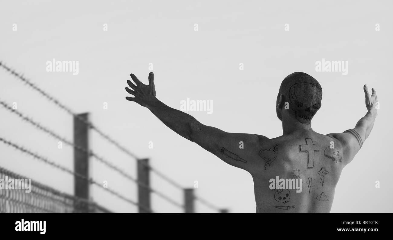 Ragazzo con doodle tatuaggi con bracci raggiunto in corrispondenza di filo spinato. Penale, convict sommossa e carcere tattoo concetto. Montaggio dell'immagine. Foto Stock