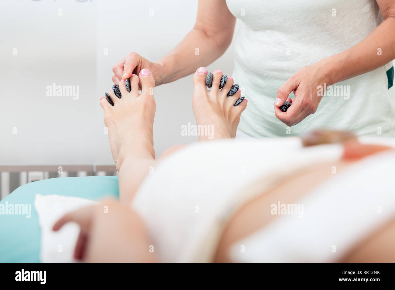 Massaggiatrice mettendo pietre nel mezzo di gambe dito Foto Stock