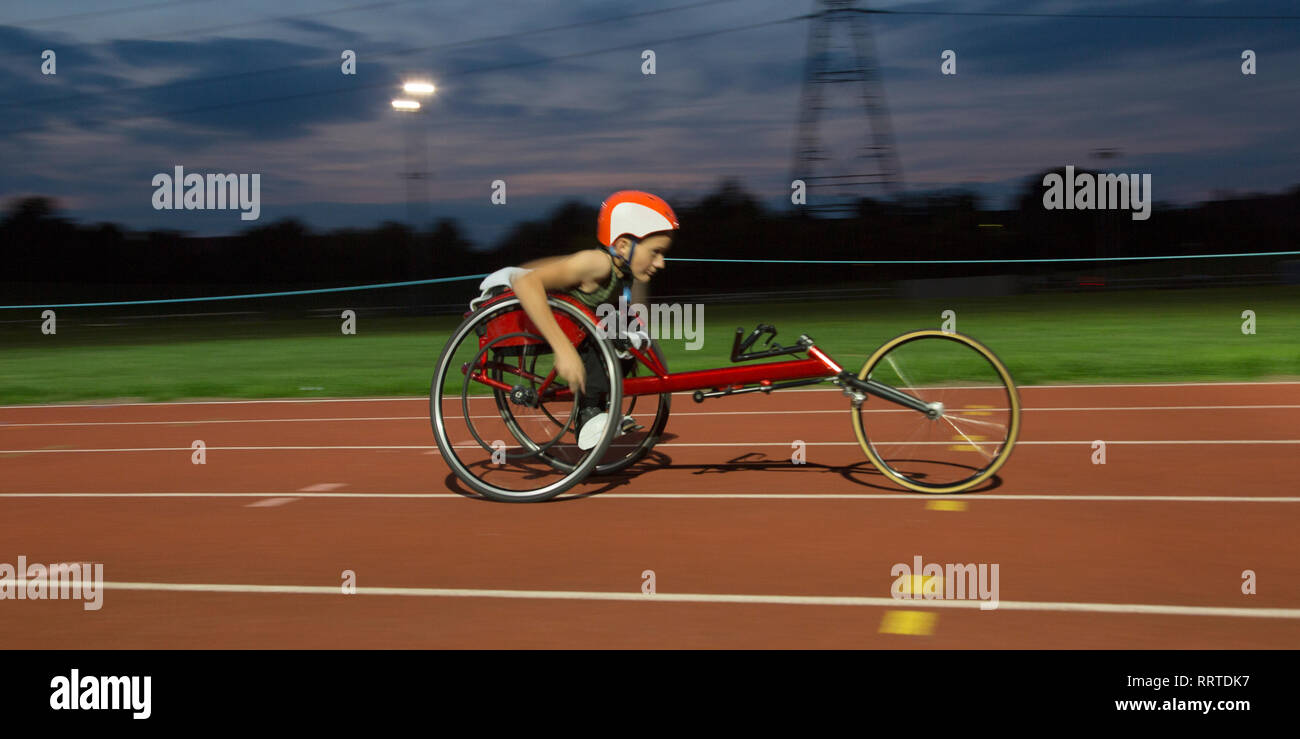 Determinata ragazza adolescente atleta paraplegico accelerando lungo la via dello sport in carrozzella gara Foto Stock