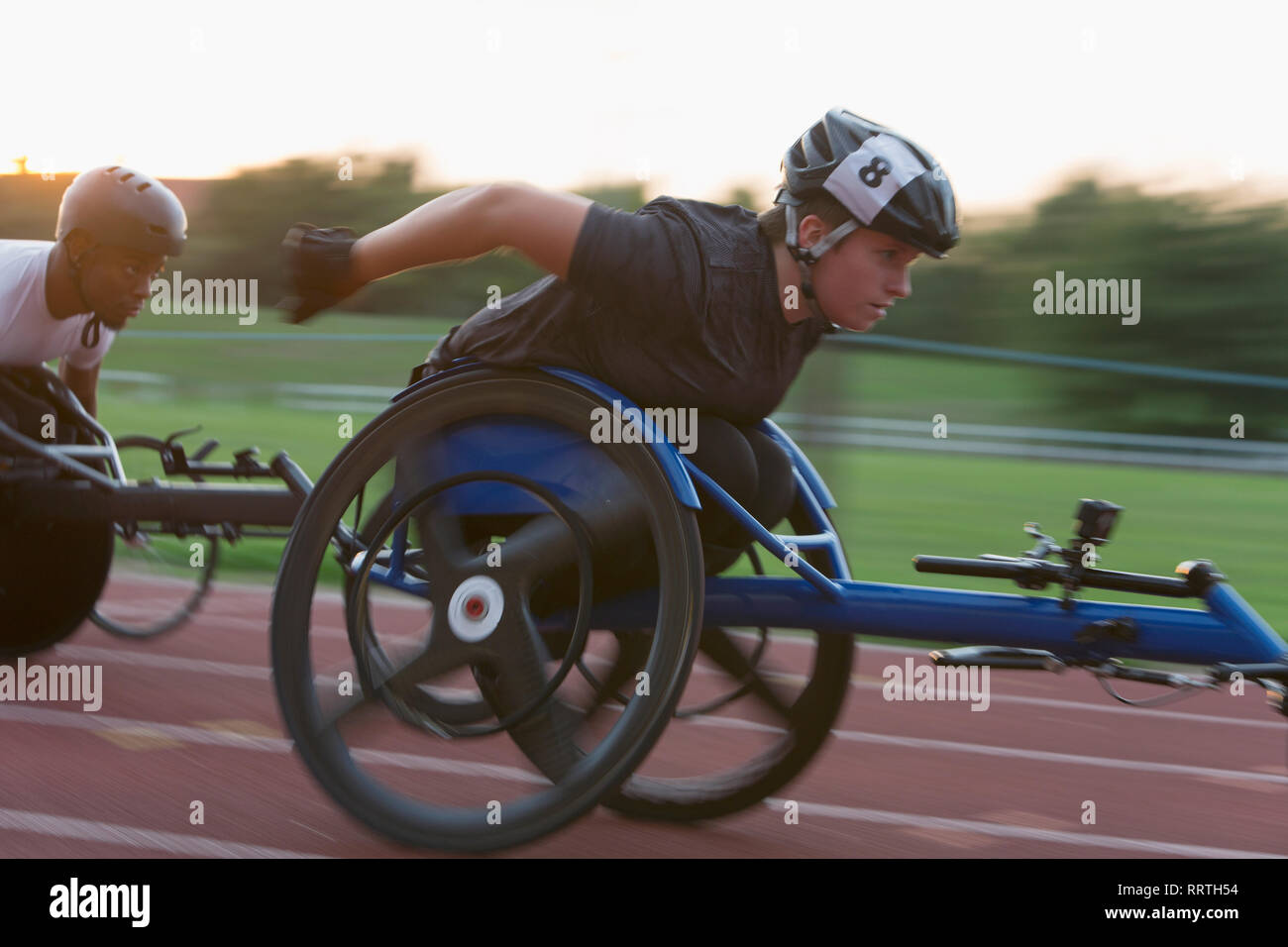 Determinata femmina e giovane atleta paraplegico accelerando lungo la via dello sport in carrozzella gara Foto Stock