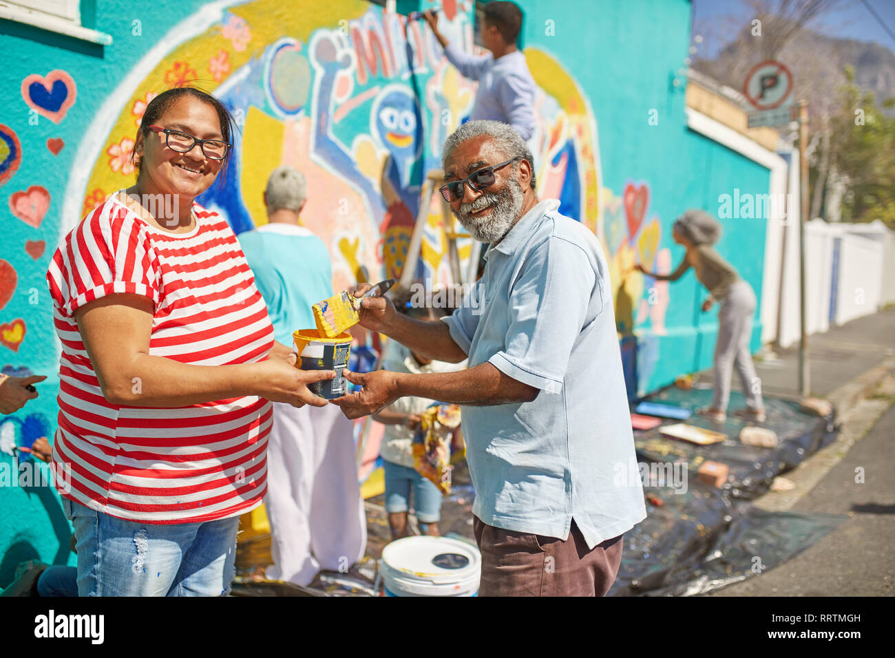 Ritratto felice volontari della comunità la pittura murale sulla soleggiata parete urbana Foto Stock