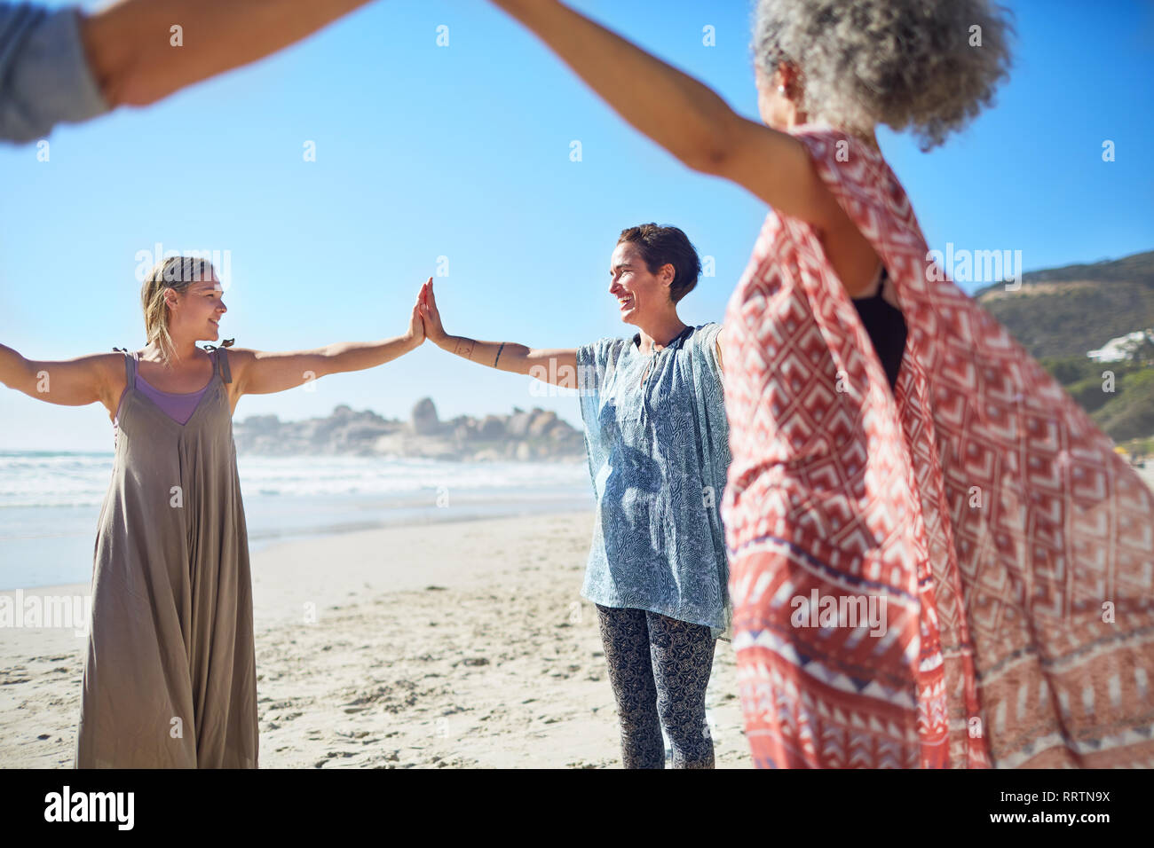 Le donne di unire le vostre mani in cerchio sulla spiaggia soleggiata durante il ritiro di yoga Foto Stock